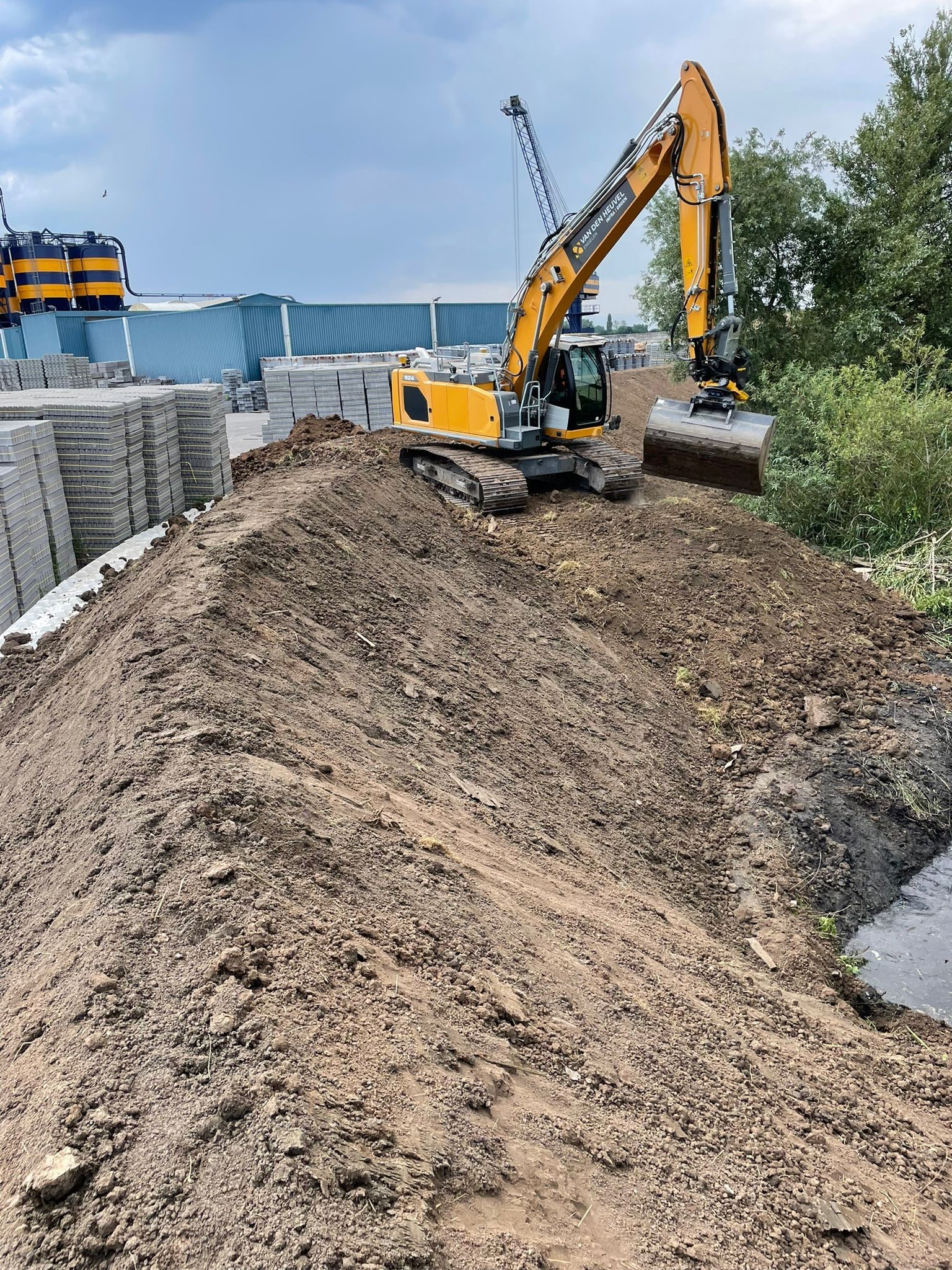 Graafmachine voert grondwerk uit op een bouwlocatie met een grote grondberg op de voorgrond